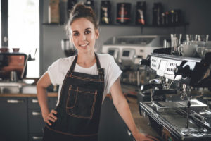 Young smiling cafe business owner standing at bar in coffee shop