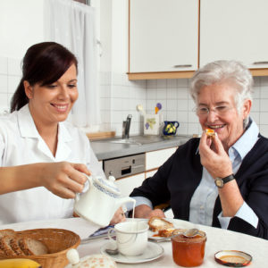 nurse helps elderly woman at breakfast